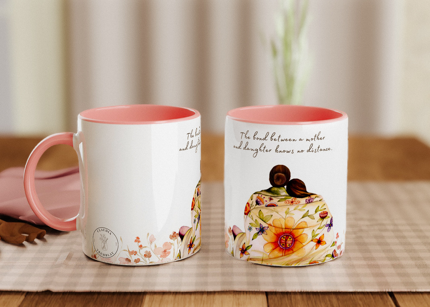 A high resolution photo of two pink mugs, one seen from the side and one from the front. They feature a mother and daughter wrapped in a floral blanket, with the quote "The bond between a mother and daughter knows no distance." inscribed above the original illusration by Claudia Tremblay.